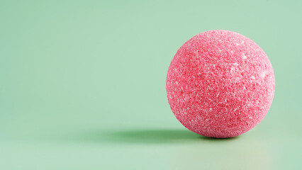Pink sea salt bath bomb on a light green background. Porous surface of the sphere. Imitation of a...