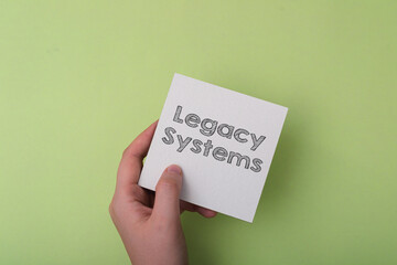 A hand holding a piece of paper with the word Legacy Systems written on it