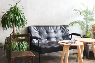 an indoor living room cafe relax area with a black sofa, two divan coffee tables, a tree and plants...