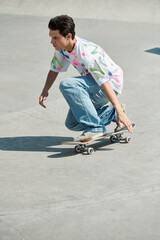 A young man confidently riding a skateboard down a cement ramp in a skate park on a sunny summer...