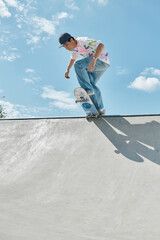 A young skater boy confidently rides a skateboard down the side of a ramp in a busy outdoor skate...
