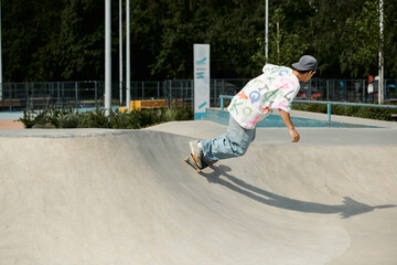 A young skater boy confidently rides his skateboard up the side of a ramp in a sunny summer skate...