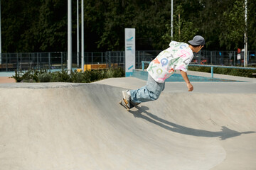 A young skater boy confidently rides his skateboard up the side of a ramp in a sunny summer skate park.