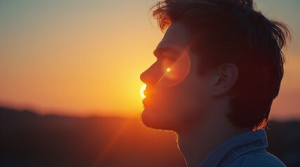 A young man with flowing hair is silhouetted against the setting sun, highlighting his peaceful expression.