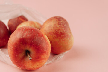 A bag of apples sits on a pink background