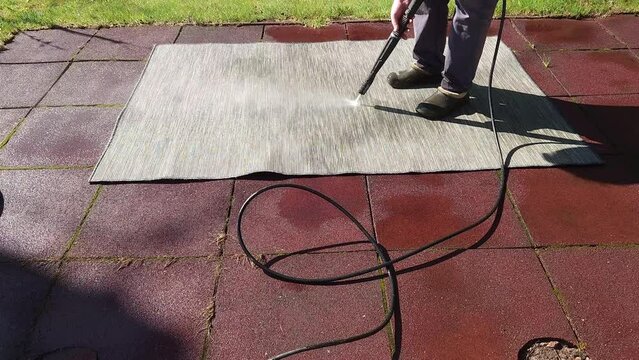 Washing carpet on rubber flooring in backyard. Man cleaning stone garden paths with high pressure power washe. Taken from hand. High quality 4k footage