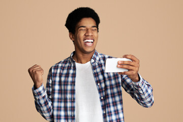 Win game. Cheerful afro guy playing games on cellphone and celebrating victory, white background