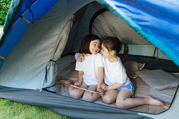 Two beautiful sisters watching cartoons playing on a tablet in a tent