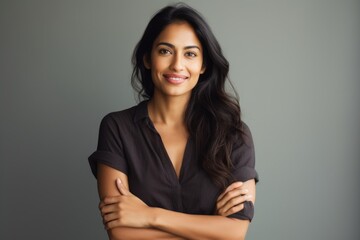 Portrait of a blissful indian woman in her 30s with arms crossed while standing against light wood minimalistic setup