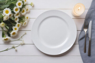 A white wooden table, with a plate, surrounded by flowers and cutlery and a lit candle, top view, with space for text.