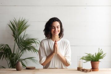 Portrait of a satisfied woman in her 30s joining palms in a gesture of gratitude isolated in light wood minimalistic setup