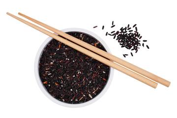 a cup of uncooked black rice grains with a pair of chopsticks and some scattered over isolated...