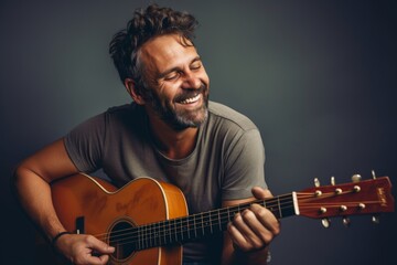 Portrait of a grinning man in his 40s playing the guitar on light wood minimalistic setup
