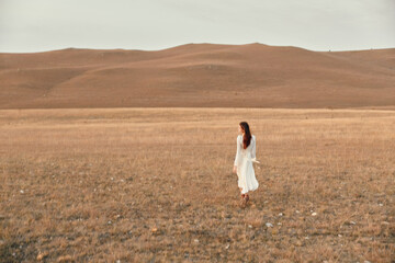 Woman walking through open field with hills in the background on travel adventure beauty journey...