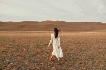 Woman walking in serene white dress through open field with hills in the background nature and...