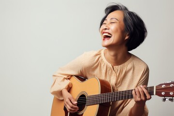Portrait of a happy asian woman in her 50s playing the guitar isolated on light wood minimalistic setup