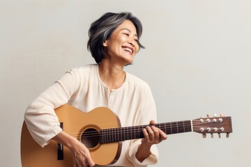Portrait of a happy asian woman in her 50s playing the guitar on light wood minimalistic setup