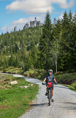active senior woman on a bike packing tour with her electric mountain bike in the summit area of Dresessel Mountain in the Bavarian Forest near Neureichenau, Bavaria, Germany