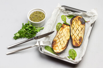Grilled baked eggplants on pallet. Fork and knife. Mash in bowl and parsley sprigs