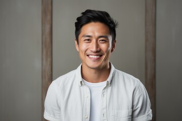 Obraz premium Portrait of a smiling asian man in his 20s smiling at the camera over light wood minimalistic setup