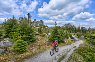 active senior woman on a bike packing tour with her electric mountain bike in the rocky the summit of Great Arber in the Bavarian Forest, Bavaria, Germany