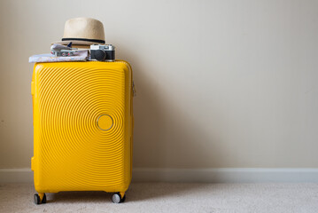 Yello suitcase with airplane, hat and camera against the wall. travel concept. minimal style