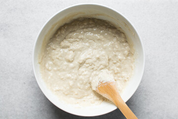 Overhead view of nigerian puff-puff dough being mixed with a wooden spoon, puff-puff dough in a...