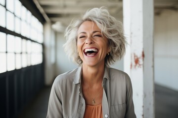 Portrait of a glad woman in her 50s laughing while standing against empty modern loft background