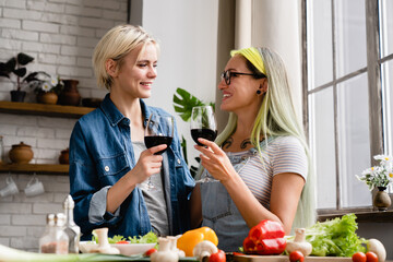 Two female couple girlfriends lesbians lgbtq women drinking wine while cooking preparing food for...