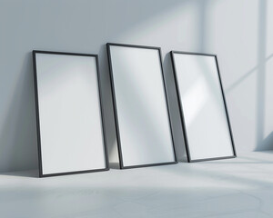 A series of three empty white frames with dark borders, spotlighted and arranged in a staggered fashion against a light gray wall