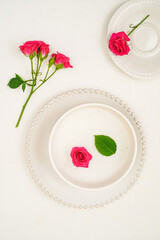 set of white plates with pink rose on white background, top view, no people