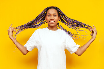 young african american woman with dreadlocks holding her hair in her hands on a yellow isolated...