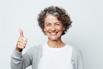 Portrait of a happy woman in her 50s showing a thumb up while standing against plain white digital canvas