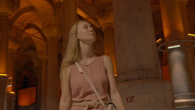 A young woman tours the ancient Cisterna of Istanbul, an underground marvel once filled with fresh water reserves, exploring its historic depths and serene ambiance. Slowmotion video.