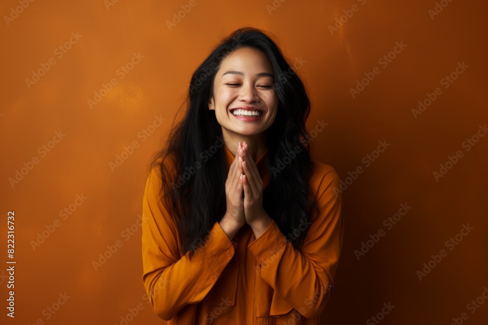 Wall mural Portrait of a happy asian woman in her 30s joining palms in a gesture of gratitude isolated in bare monochromatic room - Wall murals