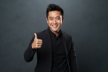 Portrait of a tender asian man in his 30s showing a thumb up isolated on bare monochromatic room