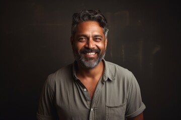 Obraz premium Portrait of a content indian man in his 40s smiling at the camera in bare monochromatic room