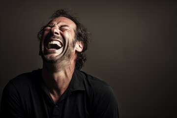 Fototapeta premium Portrait of a grinning man in his 40s laughing while standing against bare monochromatic room