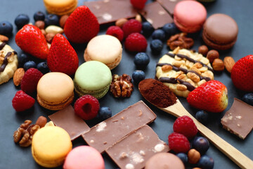 Macarons, chocolate, cookies, berries and various nuts on dark blue background. Selective focus.