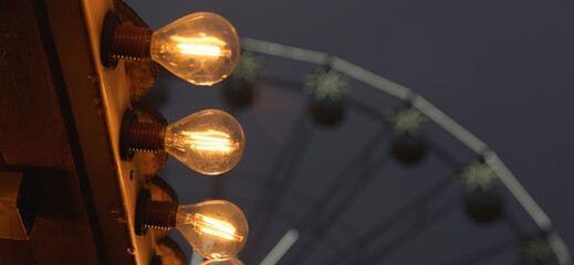 A lighted up sign with three bulbs and a Ferris wheel in the background