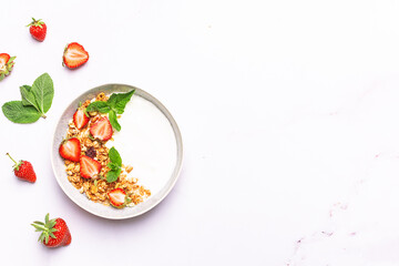 Greek yogurt with granola and fresh fruit on white marble background top view. Healthy tasty homemade breakfast concept.
