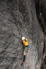 A man is climbing a rock wall with a yellow jacket and a white helmet