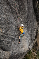 A man is climbing a rock wall with a yellow jacket and a helmet