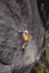 A man is climbing a rock wall with a yellow jacket and a helmet