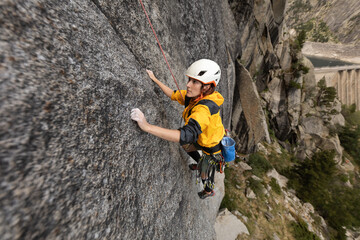 A woman is climbing a rock wall wearing a yellow jacket and a helmet