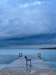The chair stands on the edge of the pier against the background of dark clouds
