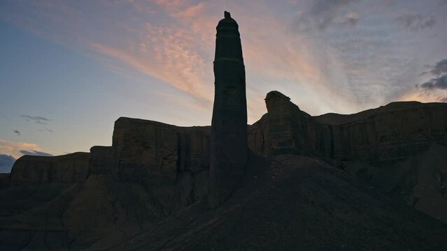 Aerial turning view of silhouette of pinnacle rock formation in desert at sunset / Caineville, Utah, United States