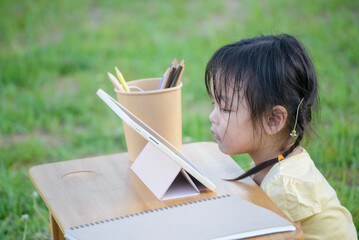 Asian preschool children using digital tablet with stylus pen write and do homework outdoor. Thai...