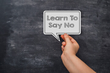 A hand holding a white paper with the words learn to say no written on it
