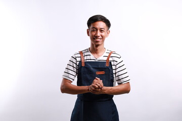 Asian attractive chef wearing a white shirt and blue apron standing with his hands clasped against...